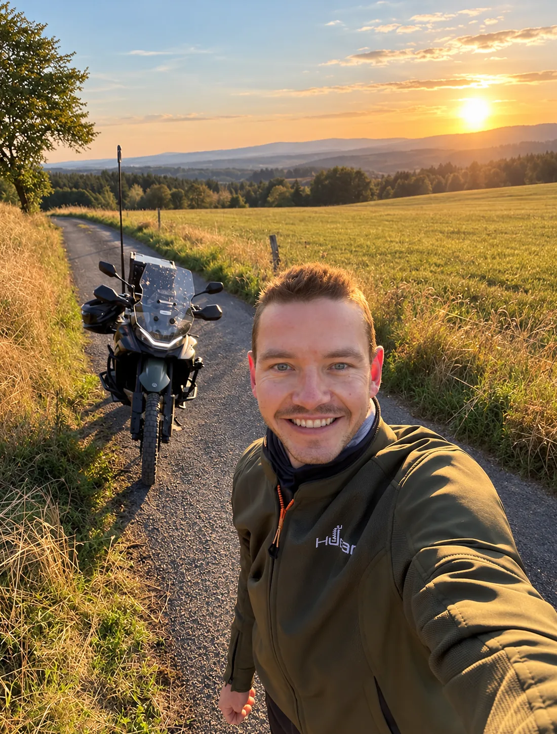 Honza Hauzr u motorky na polní cestě při západu slunce